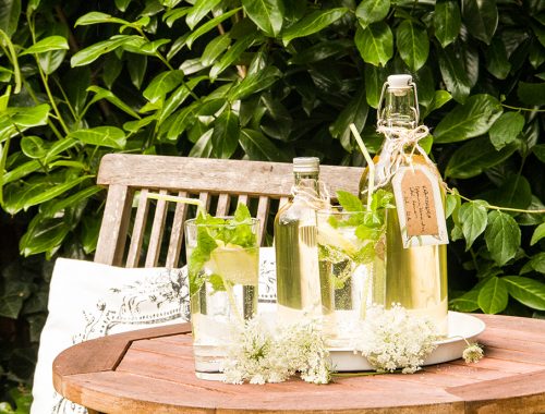 Kräutersirup in Flaschen und Gläsern auf Gartentisch